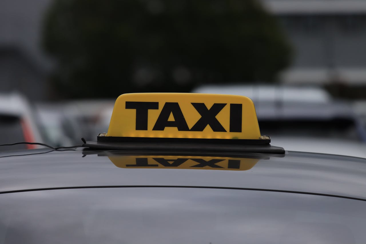 Yellow taxi sign on a car roof in a city parking area during daylight.